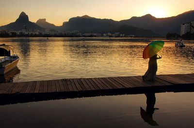 Silhouette woman standing by lake against sky during sunset