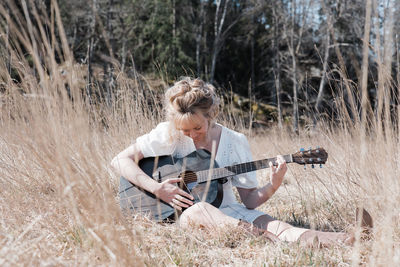 Woman sat in a field happily playing guitar in summer