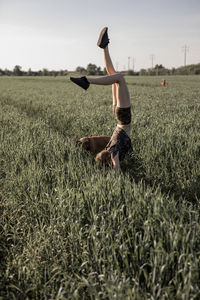 Woman doing handstand by dog on grassy field