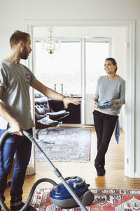 Man using vacuum cleaner while talking to woman at home