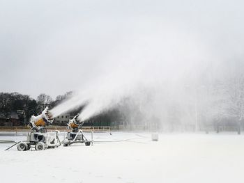 Two yellow snow blowers working on snow for cross country skiing slope in the city park at daylight