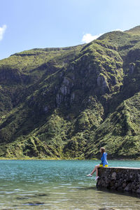 Woman sitting on retaining wall against mountain