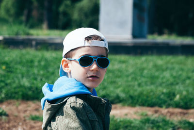 Portrait of boy wearing sunglasses and cap looking over shoulder outdoors