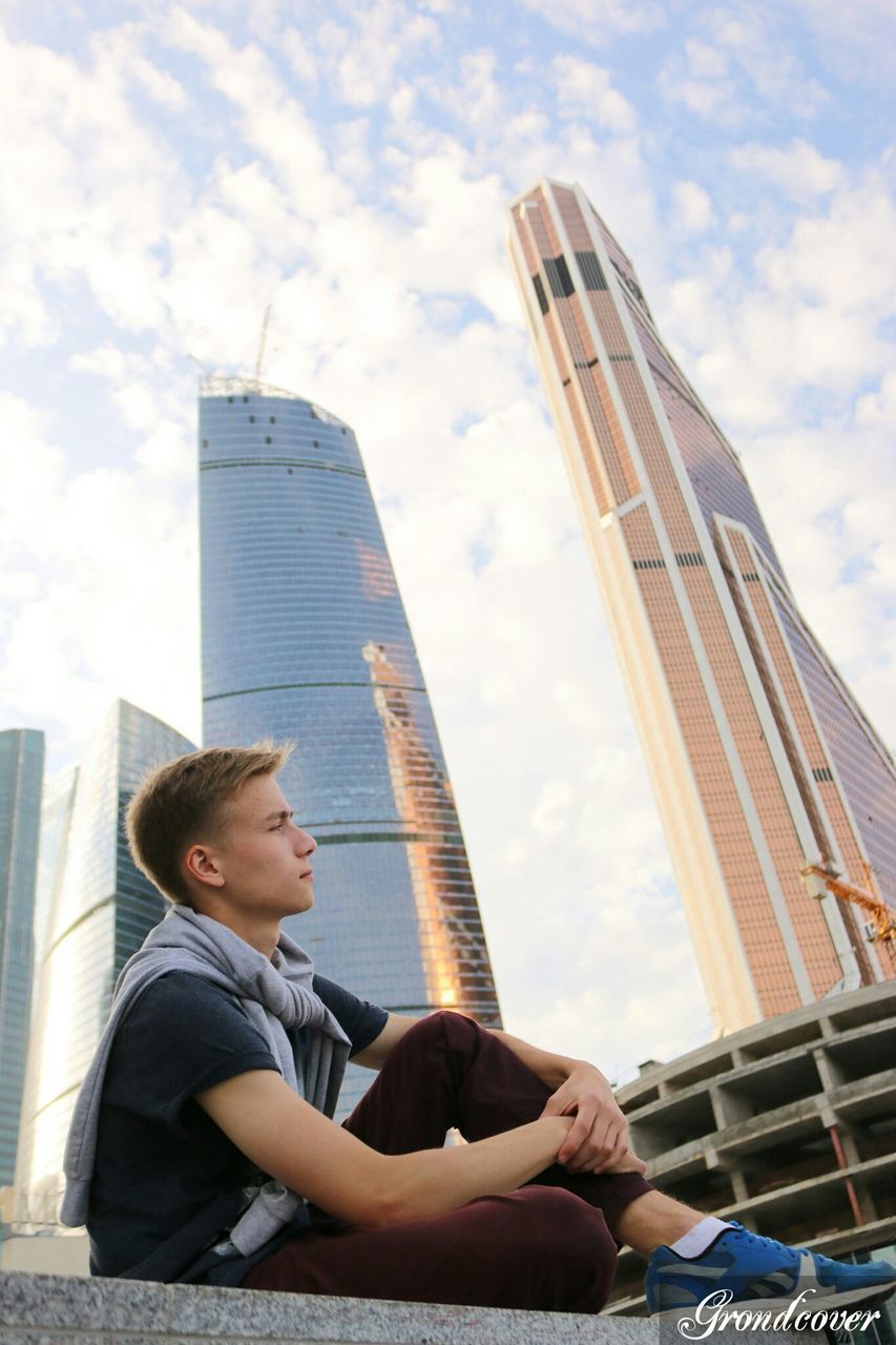 lifestyles, leisure activity, sky, architecture, built structure, low angle view, building exterior, tall - high, modern, skyscraper, city, casual clothing, wireless technology, holding, men, tower, sitting, cloud - sky