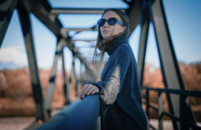 Young woman wearing sunglasses on railing against sky