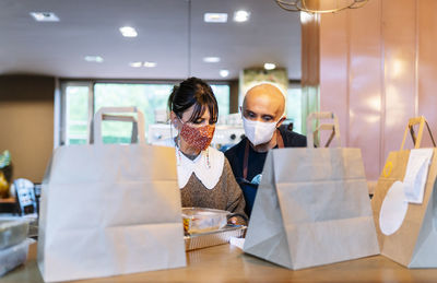 Female owner with male colleague preparing take out food on bar counter during pandemic