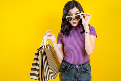 Young woman wearing sunglasses standing against yellow background