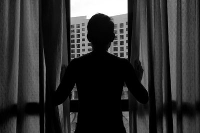 Rear view of silhouette man standing in front of window