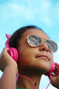 Portrait of girl wearing sunglasses and headphones against sky 