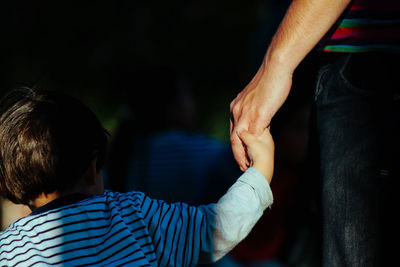 Midsection of father holding son hand in sunny day