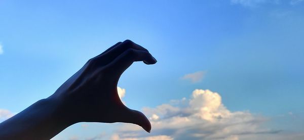 Low angle view of hand holding statue against sky