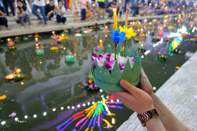 Cropped hands of woman holding religious offering against pond