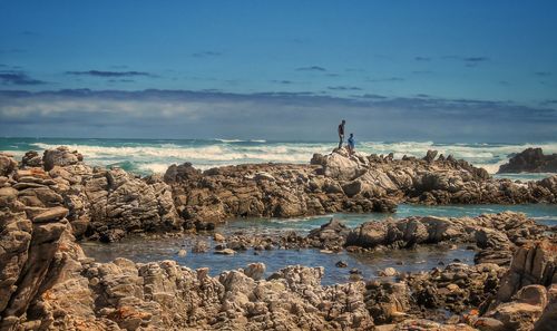 Man standing on rock by sea against sky