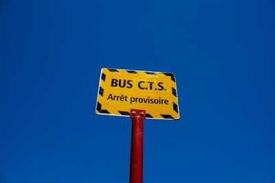 Low angle view of road sign against clear blue sky