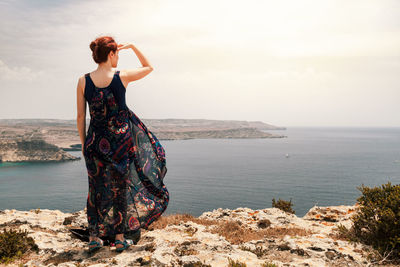 Rear view of woman standing on cliff against sea