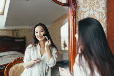 Beautiful woman applying lipstick in front of mirror at home