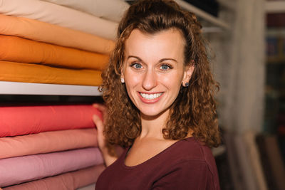 Young woman with curly hair and a bright smile choosing fabric rolls in a vibrant craft store