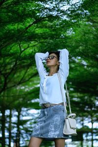 Young woman wearing sunglasses while standing against trees