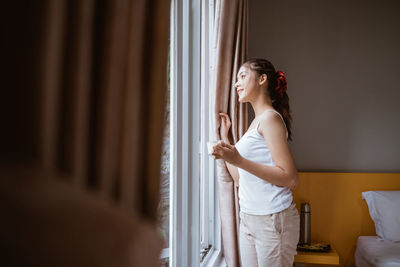 Side view of young woman standing against curtain