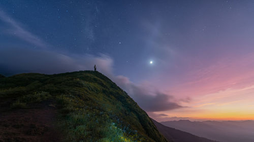 Distant view of man standing on mountain against sky at dusk