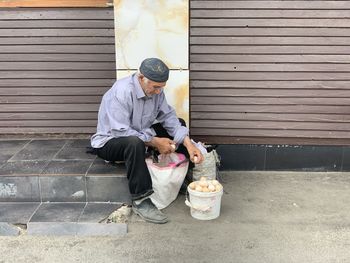 Full length of man sitting on footpath