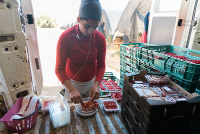 Attentive female gardener measuring weight of ripe raspberries on digital scales in van trunk