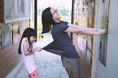 Side view of girl pulling mother locking window