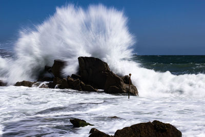 Sea waves splashing on rocks against sky