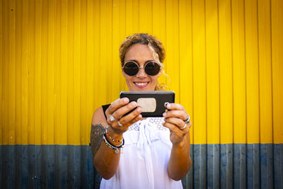 Smiling woman holding smart phone against wall outdoors