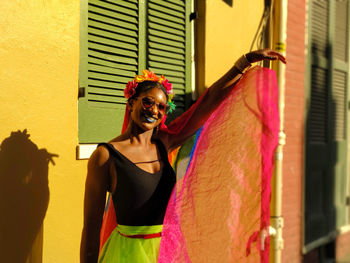 Smiling woman holding scarf while standing against wall