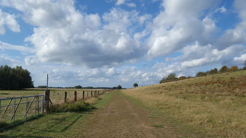 Scenic view of road amidst field against sky