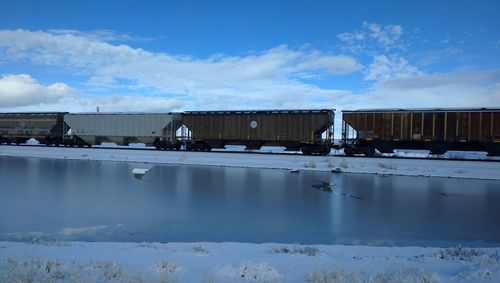 Cargo train by lake against sky during winter