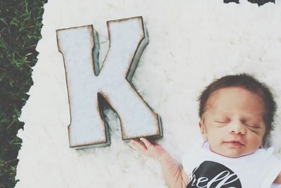 Directly above shot of baby boy sleeping by letter k on rug