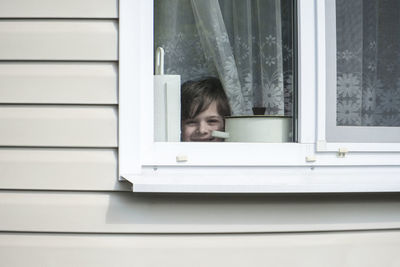 Portrait of happy and cheerful boy looking at the camera through the window.