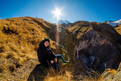 Young woman sitting on rock against sky