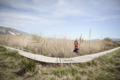 Girl jumping on boardwalk against sky