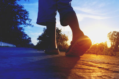 Low section of man walking on street during sunset 