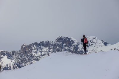 Man walking on snowcapped mountain against sky during winter
