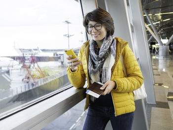 Smiling woman with passport, boarding pass is texting on her smartphone.tourist waits for boarding