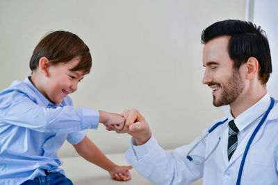 Cheerful doctor and boy bumping fist at hospital