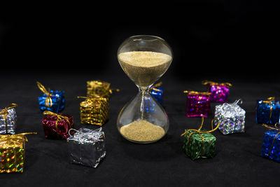 Close-up of hourglass by gifts against black background
