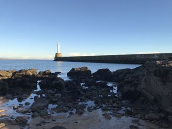 Lighthouse by sea against clear sky