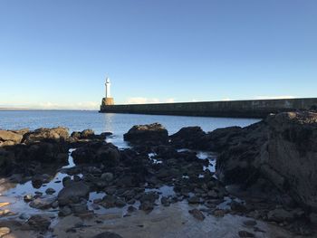 Lighthouse by sea against clear sky