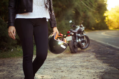 Midsection of woman standing with helmet by motorcycle