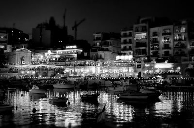 Boats moored in river against illuminated city at night