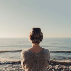 Rear view of woman standing at beach against clear sky