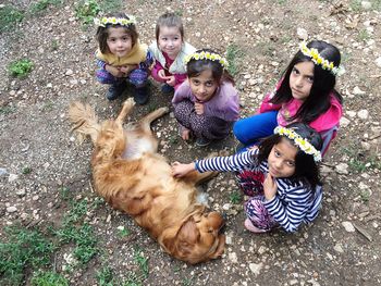 High angle portrait of girls crouching by golden retriever lying ground