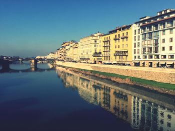 Reflection of buildings in river against clear blue sky