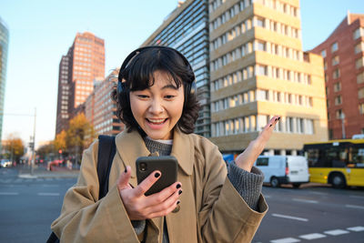 Portrait of young woman using mobile phone in city