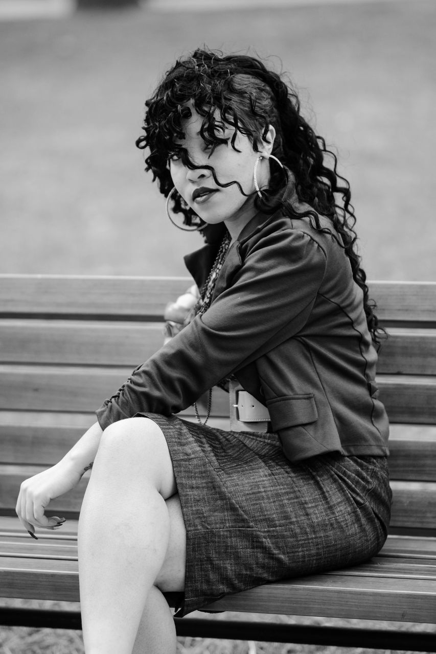 sitting, one person, real people, leisure activity, lifestyles, looking away, casual clothing, full length, day, looking, contemplation, bench, seat, young adult, women, focus on foreground, front view, hairstyle, beautiful woman, outdoors, park bench